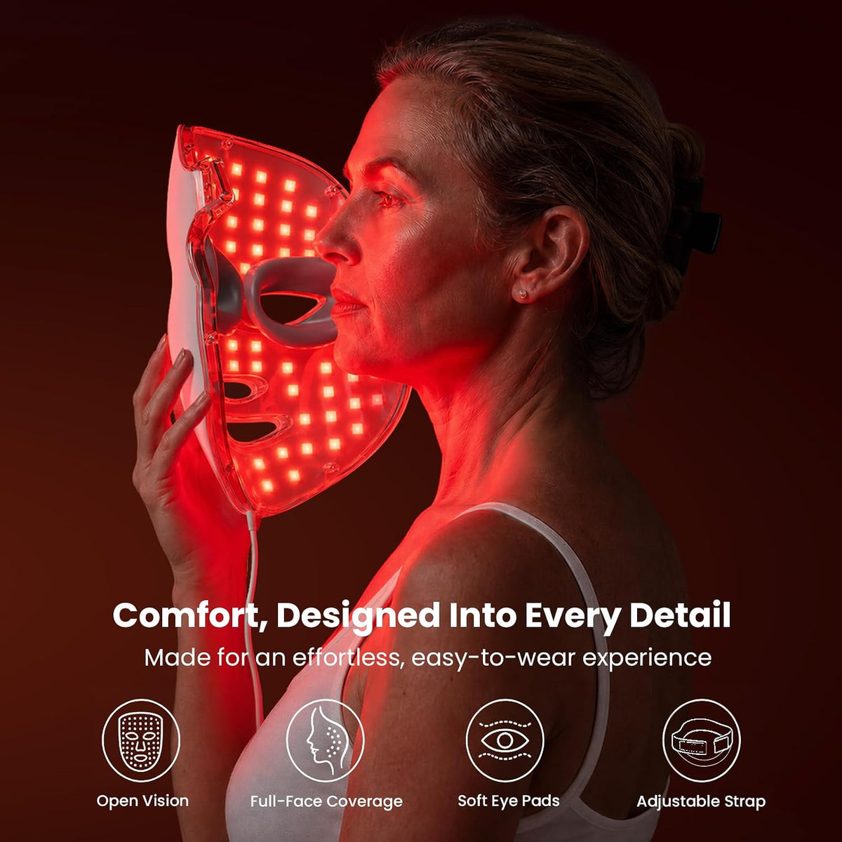 A woman wearing a red light therapy face mask, shown in profile against a dark red background. The mask is illuminated with red LED lights and features a white outer frame. Comfort, Designed Into Every Detail: Made for an effortless, easy-to-wear experience. Includes open vision, full-face coverage, soft eye pads, and an adjustable strap.