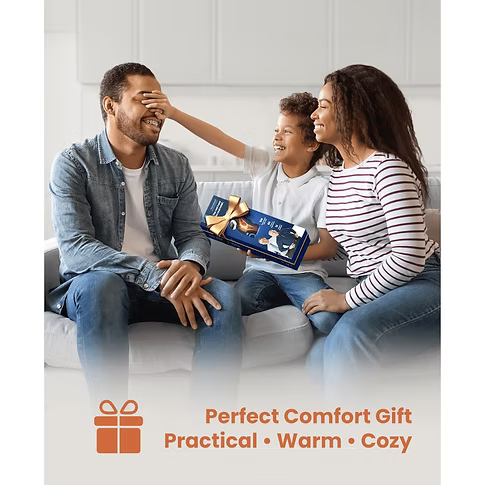 A family of three sits on a light-colored sofa in a bright living room, with the mother holding a blue box with the Bob and Brad TheraHeat Knee Brace wrapped in gold ribbon. The image has a warm overlay at the bottom with the text 'Perfect Comfort Gift Practical • Warm • Cozy' and an orange gift box icon.
