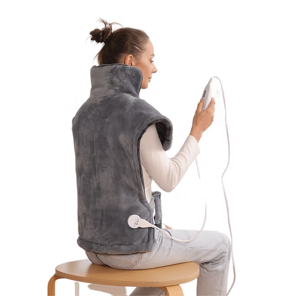 A woman seated on a wooden stool, shown from the back and side, wearing a gray heating pad and holding a white handheld controller with a cord. The photo is shot against a clean white background.