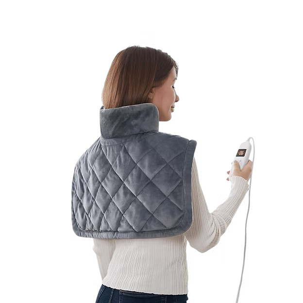 A woman shown from the back wearing a gray quilted neck and shoulder heating pad, holding a white remote control against a plain white background.