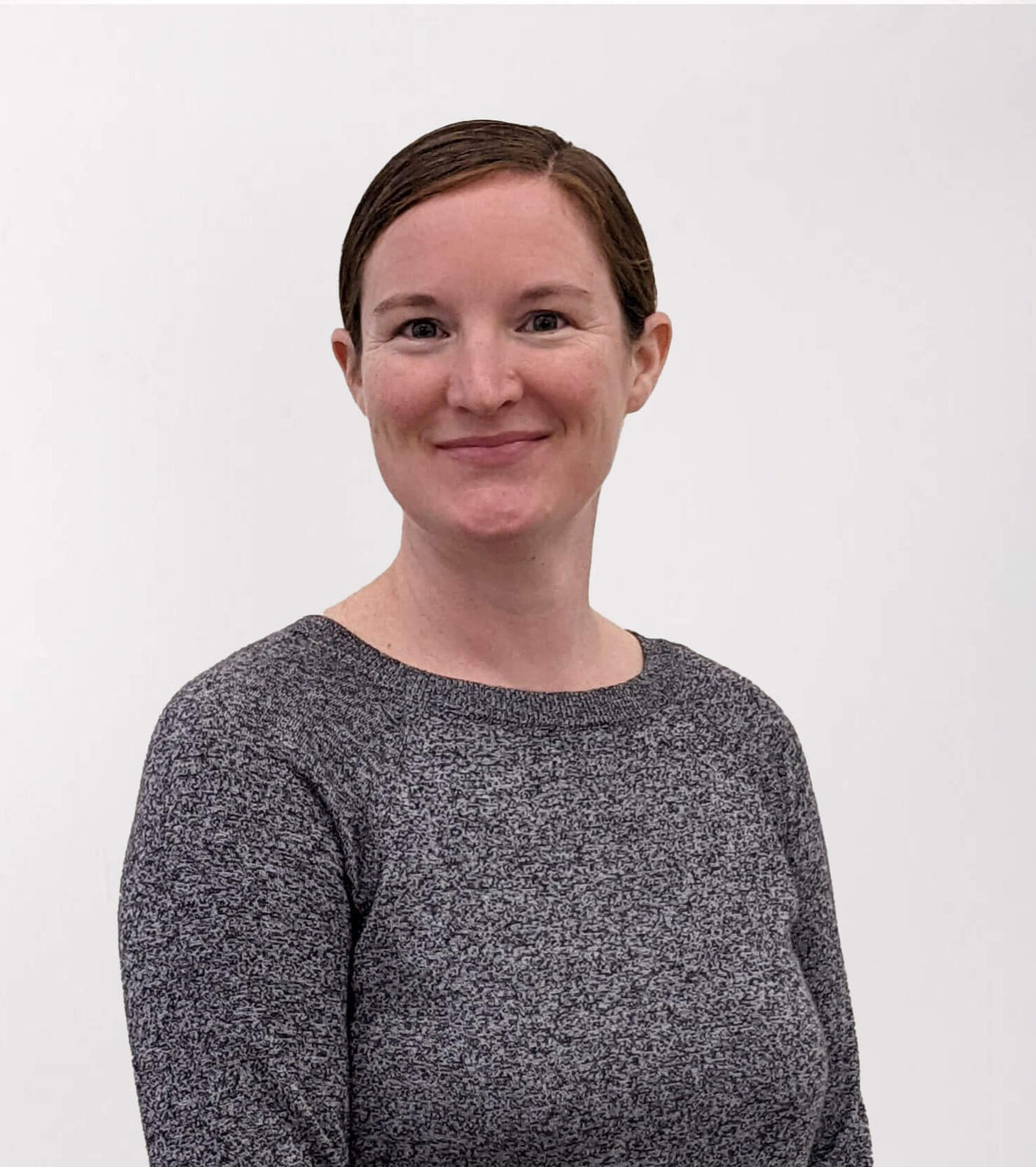 Chelsie with brown hair pulled back, wearing a heathered dark gray long-sleeve knit top, photographed against a plain light gray background.
