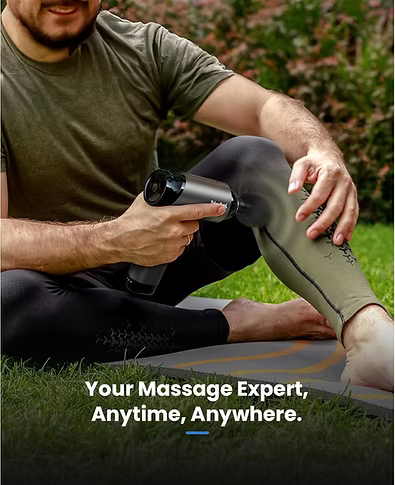 A man sitting on the grass outdoors uses a handheld massage gun on his leg. He is wearing an olive green T-shirt and black leggings, with a yoga mat underneath. Text includes: Your massage expert, anytime, anywhere. 